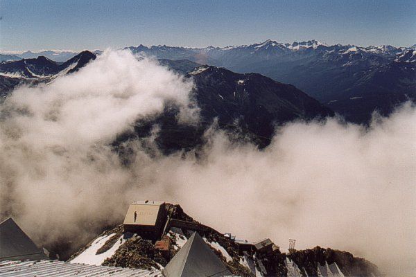 Guardando verso il basso sul versante italiano si vedono i due rifugi Torino, il Vecchio in basso e il Nuovo più in alto, con la tremenda scala coperta a doppia pendenza che li collega.