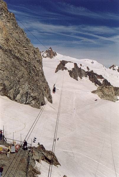 Prima di risalire sulla funivia, ammiriamo in direzione della Francia il percorso, col pilone sospeso, il passaggio sul Gros Rognon (con cambiamento del cavo portante nonchè leggera deviazione) e in fondo la sagoma dell'Aiguille du Midi.