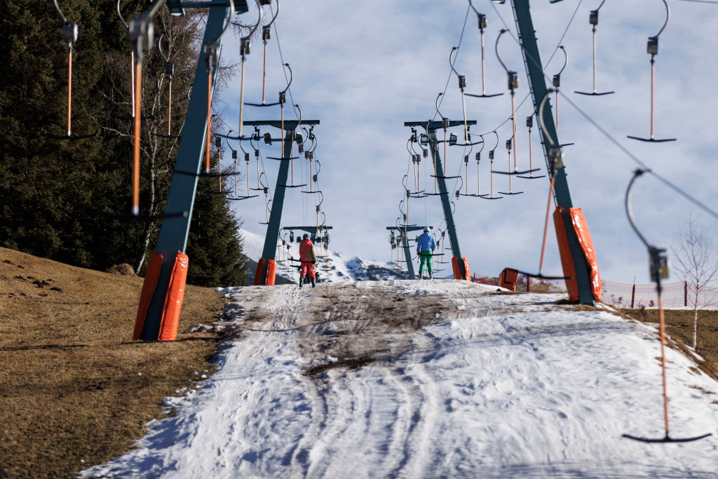 Skiers ride a ski lift on a track covered in artificial snow